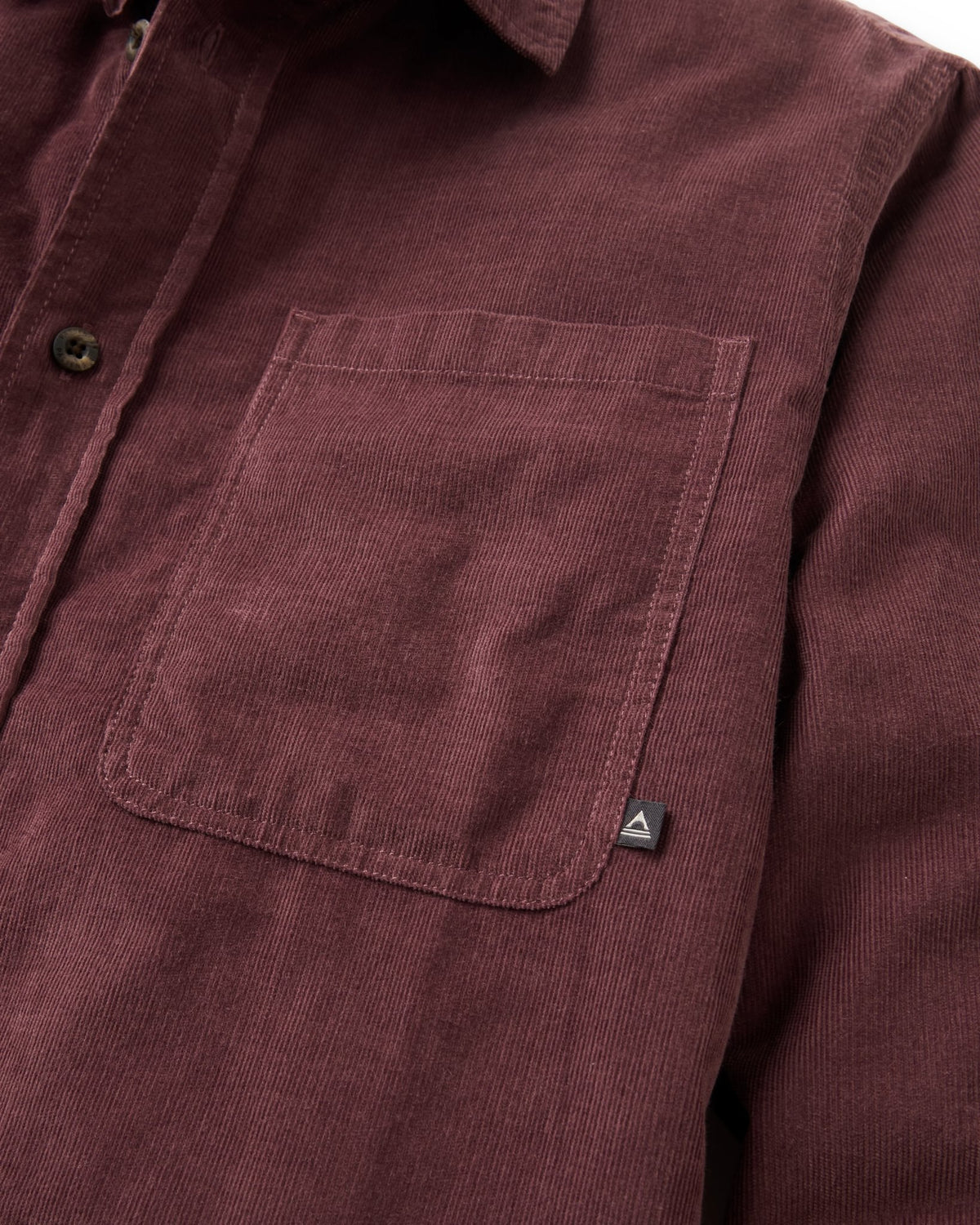Close-up of a corduroy button-up shirt in a deep burgundy color, showing the chest pocket and a small triangular logo tab.