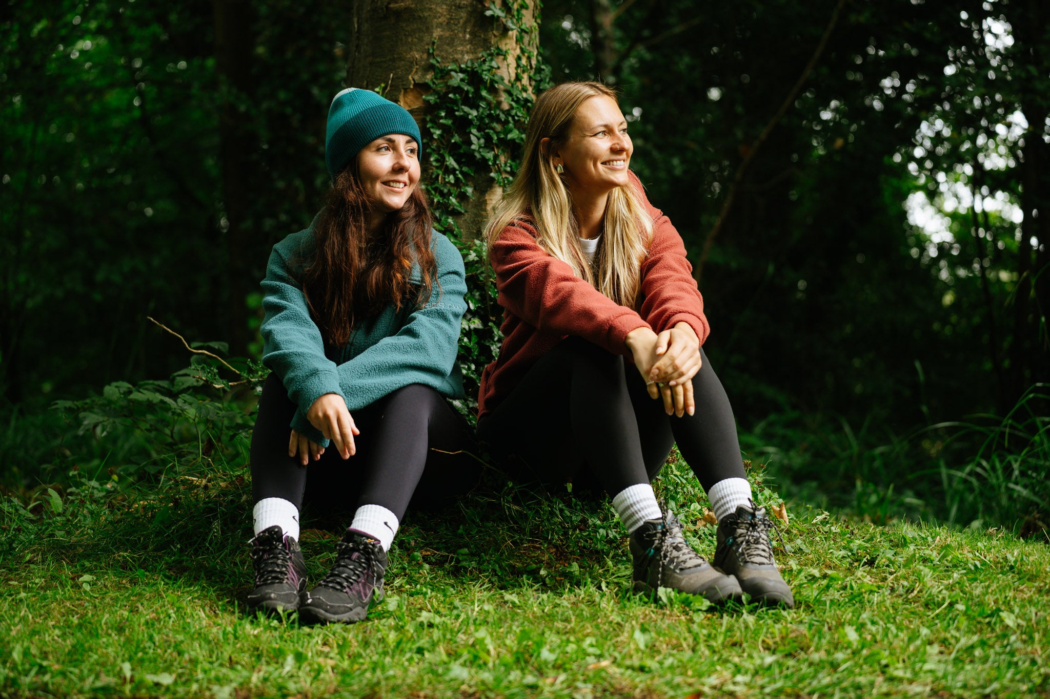 Two women sitting on the grass in a forested area wearing Portwest Outdoor Clothing